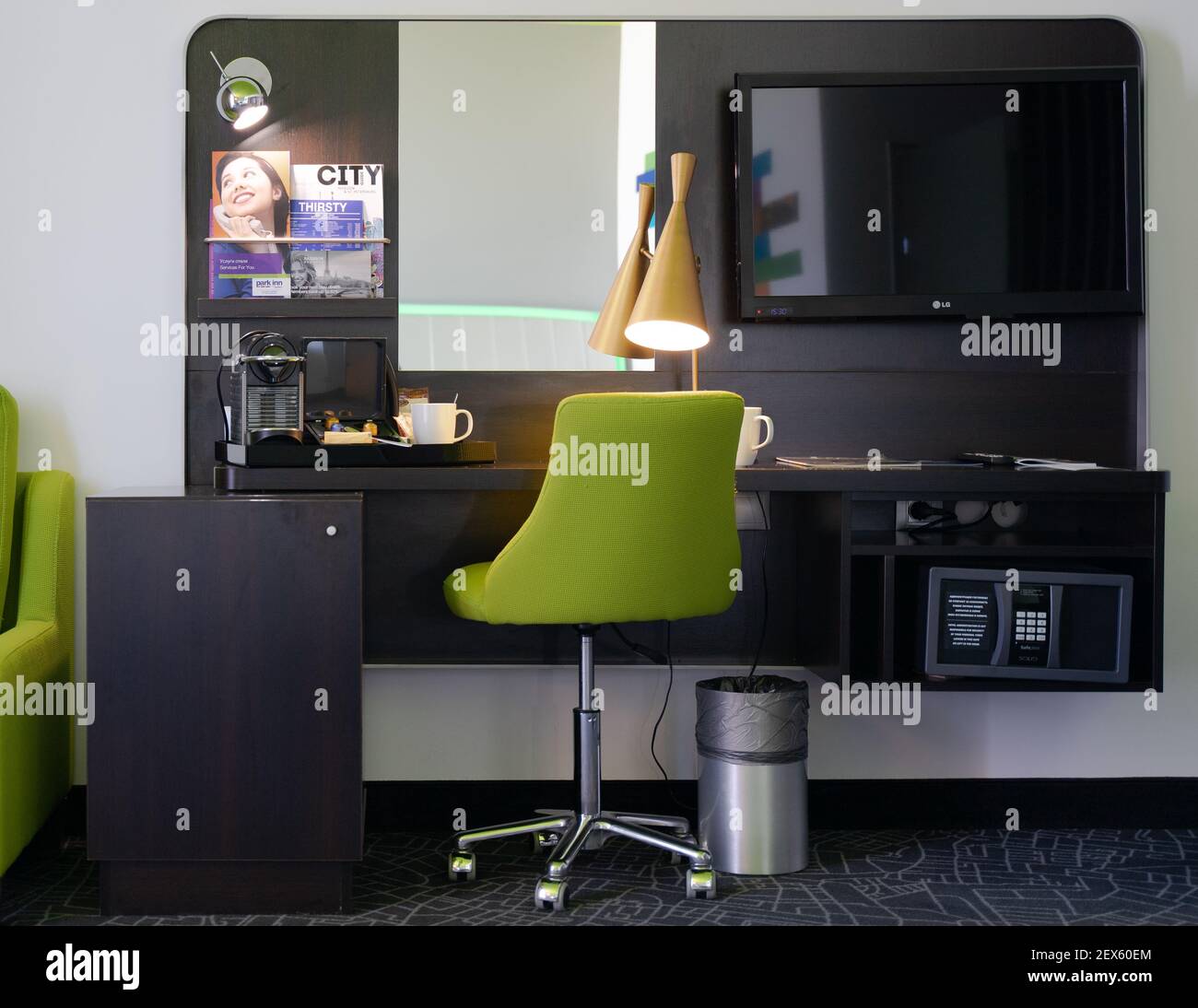 Un posto moderno per lavoro e affari nella camera d'albergo, con un tavolo, sedia verde, lampada moderna, tv, cassetta di sicurezza, macchina per il caffè Foto Stock