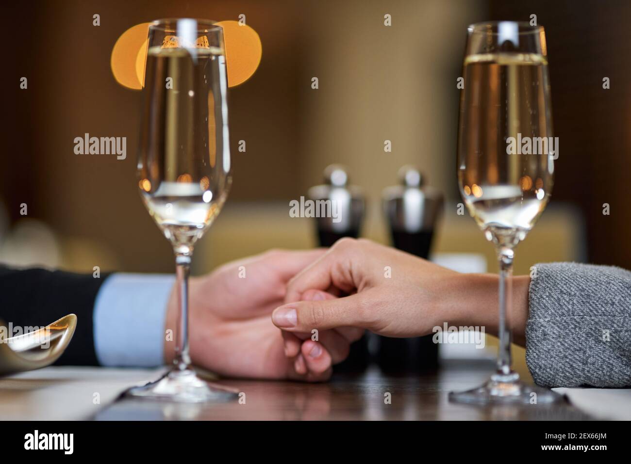 Foto ritagliata di due mani che toccano il tavolo vicino due bicchieri di champagne Foto Stock