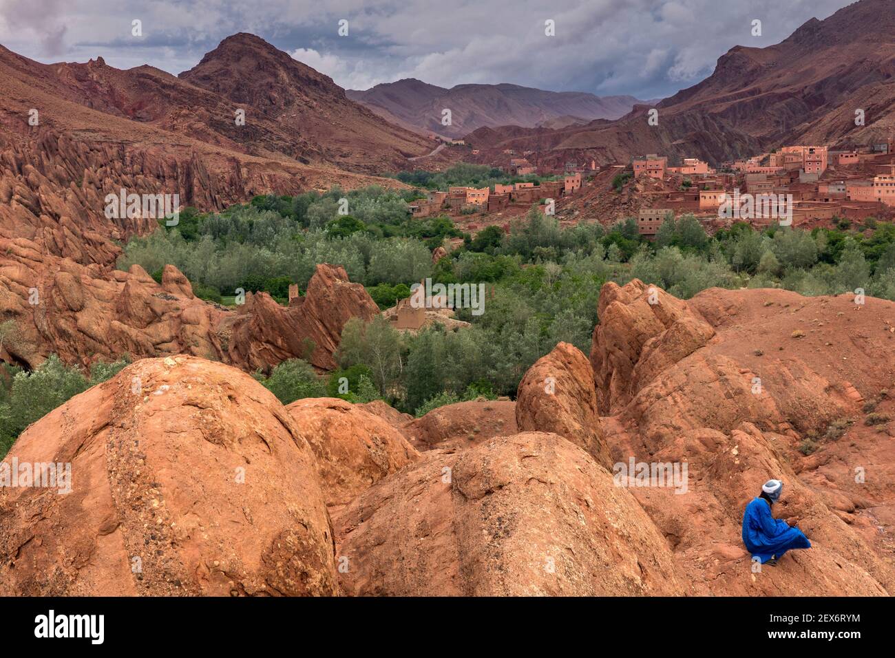 Marocco, Valle del Dades vicino alle formazioni rocciose 'Monkey Paws', con il maschio berbero vestito di blu. Un paesaggio arido con vegetazione lussureggiante lungo un fiume. Foto Stock