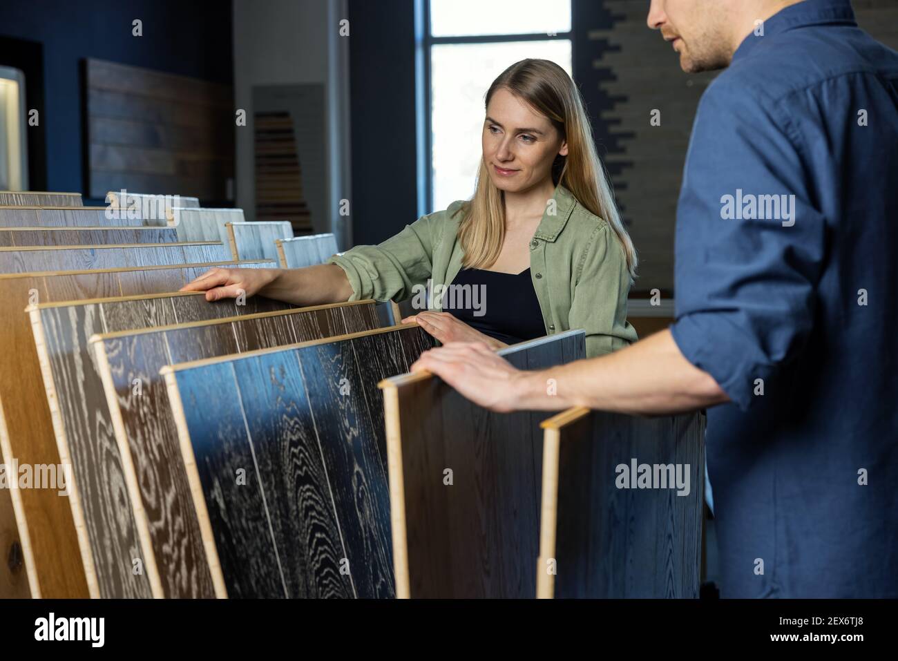 giovane coppia che sceglie pavimento laminato di tessitura di legno dai campioni dentro negozio di pavimenti per i miglioramenti della casa Foto Stock