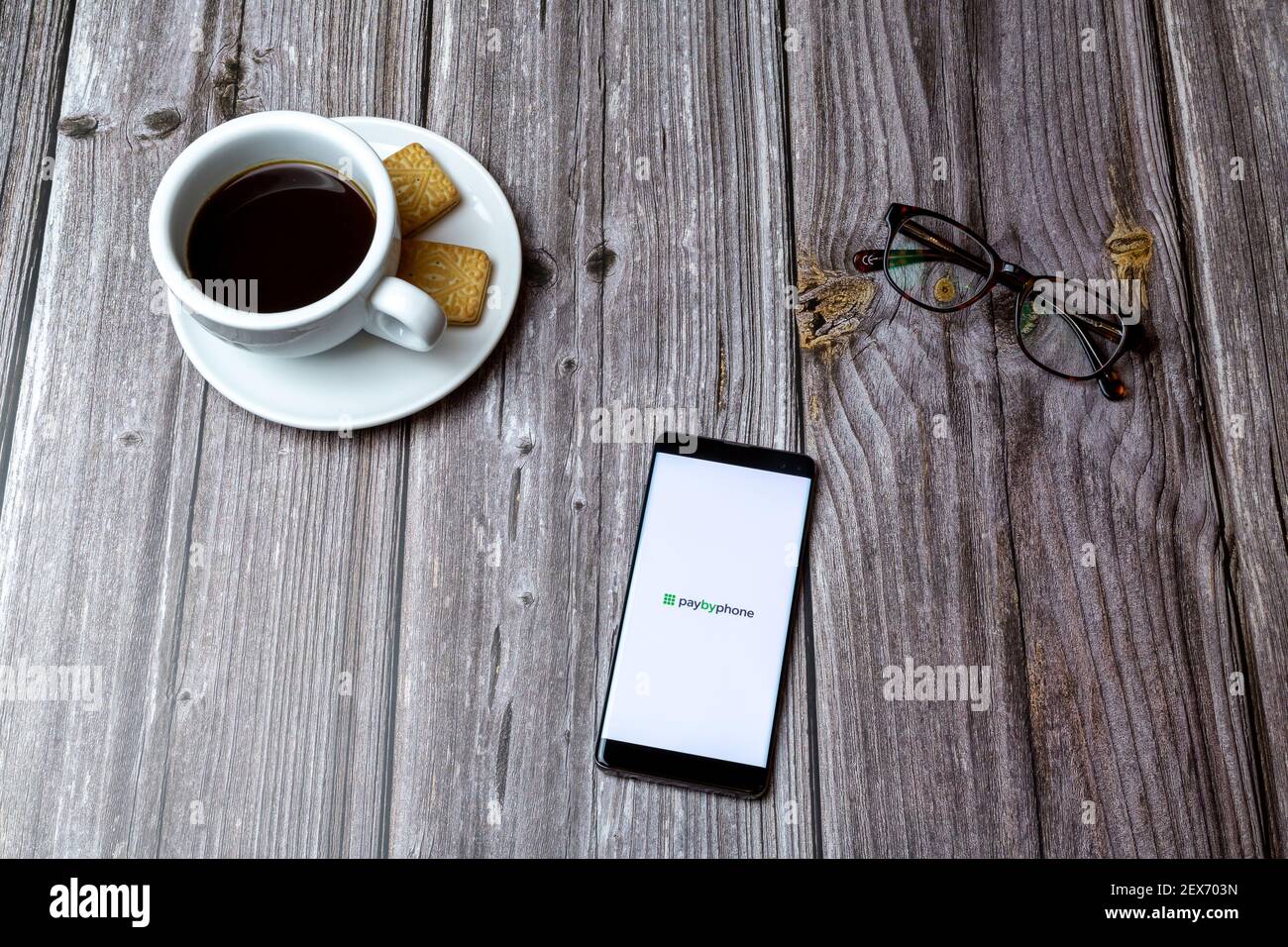 Un telefono cellulare o un telefono cellulare posato su un legno tavolo con l'app paybyphone aperta accanto a un caffè Foto Stock