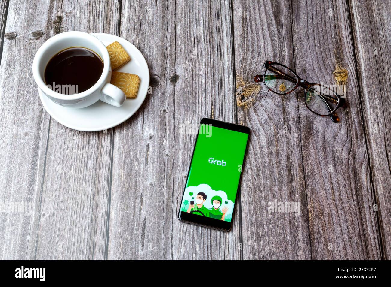 Un telefono cellulare o un telefono cellulare posato su un legno Tavolo con l'app per la consegna degli alimenti con la benna aperta accanto a. un caffè Foto Stock
