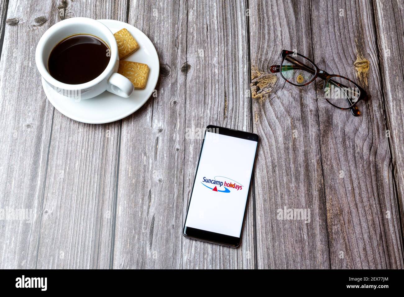 Un telefono cellulare o un telefono cellulare posato su un legno Tavolo con l'app Suncamp Holidays aperta accanto a. caffè Foto Stock