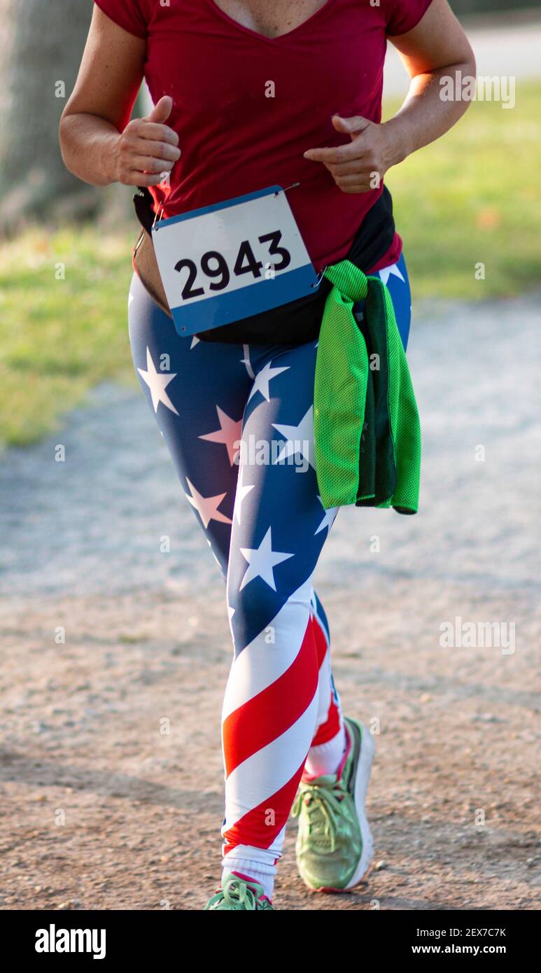Un runner zampe con spandex bandiera americana mentre si esegue una corsa 5K su un sentiero intorno a un lago. Foto Stock