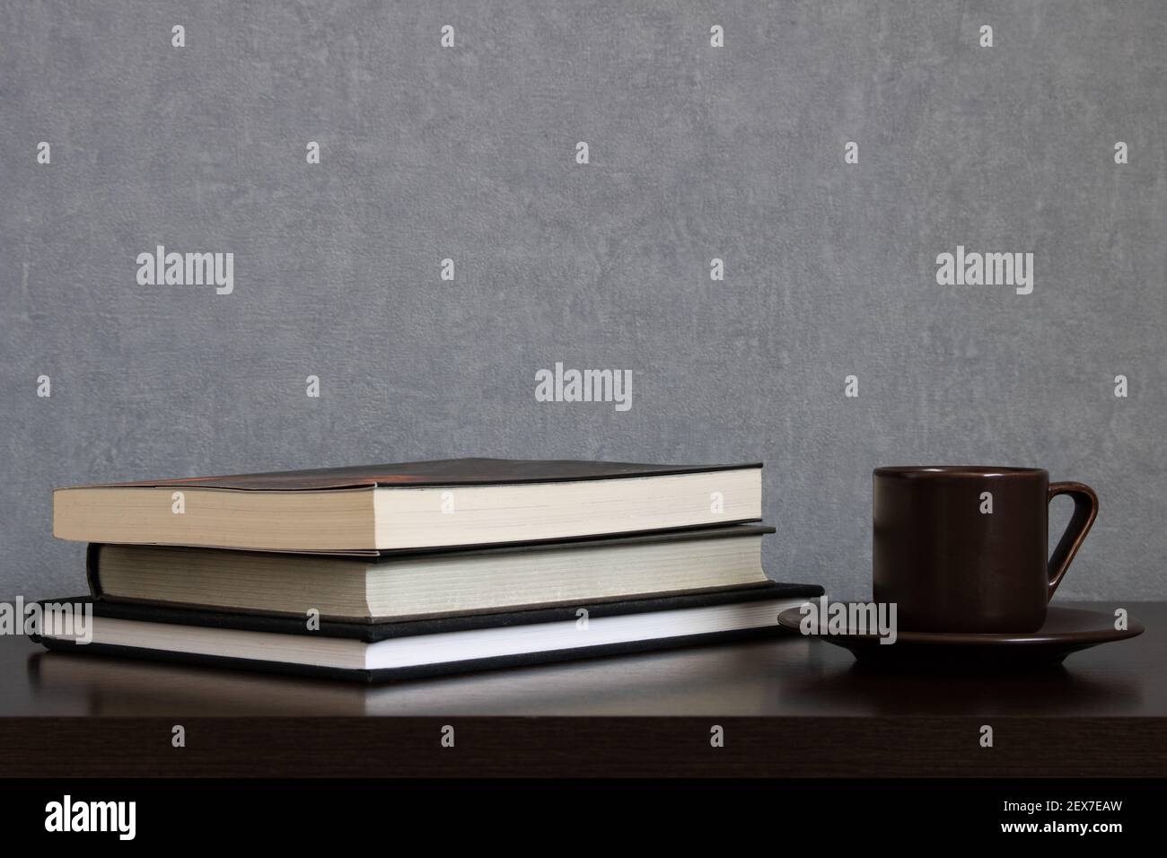 Tazza di caffè marrone con piatto accanto a un mucchio di libri da leggere su uno sfondo grigio pulito. Spazio vuoto per il testo in alto. Studiare, leggere concetti Foto Stock