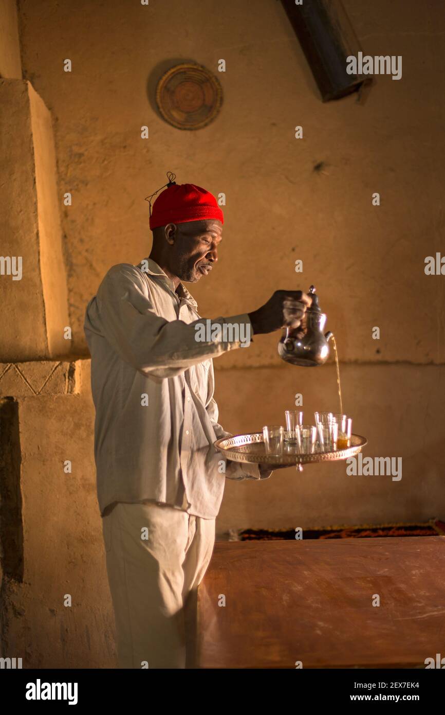 Marocco, Merzouga, ritratto di un server del tè, luce della finestra che illumina un uomo che serve il tè Foto Stock