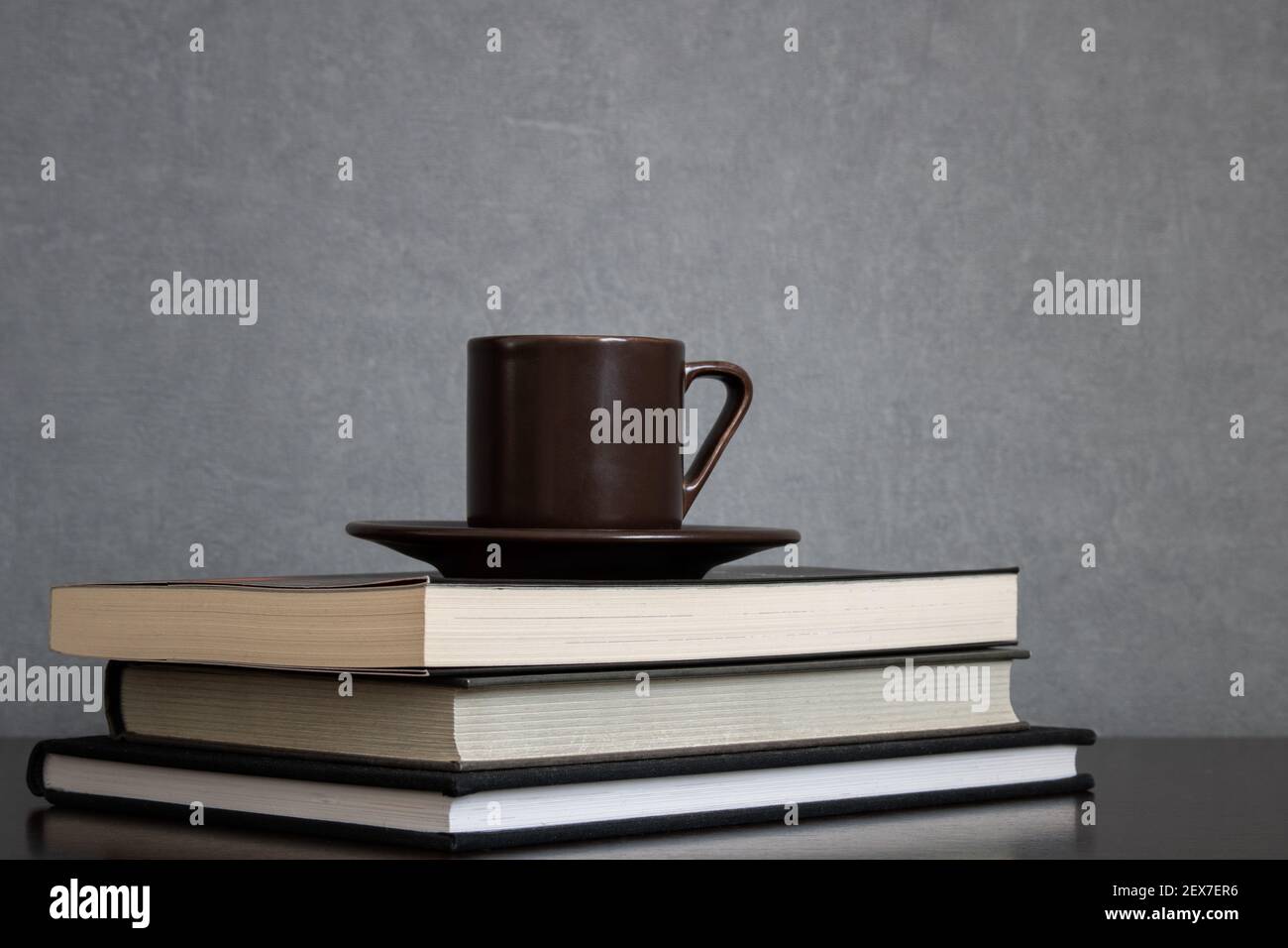 Tazza marrone di caffè con piatto sopra il mucchio di libri da leggere messo fuori centro della cornice su uno sfondo grigio pulito. Spazio vuoto per il testo Foto Stock