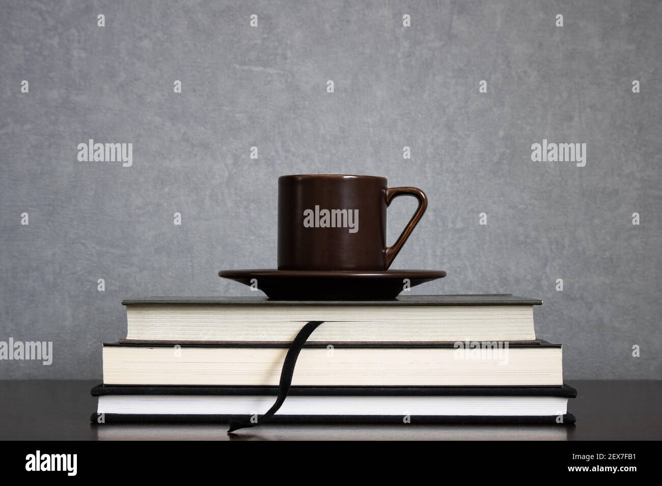 Tazza di caffè marrone con piatto sopra un mucchio di libri da leggere centrato su uno sfondo grigio pulito. Spazio vuoto per il testo. Studiare, leggere concetti Foto Stock