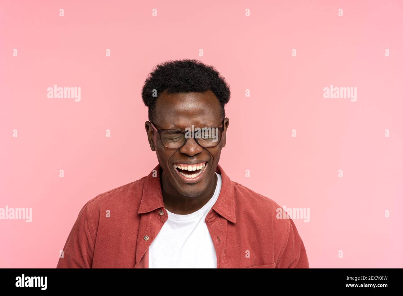 Ridendo positivo giovane afroamericano in camicia rossa di buon umore con occhi chiusi, isolato. Foto Stock