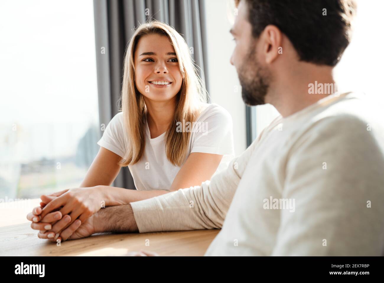 Giovane coppia innamorato che condivide un momento tenero che si aggrappano le mani mentre si siede al tavolo e sorridendo l'uno nell'altro occhi Foto Stock