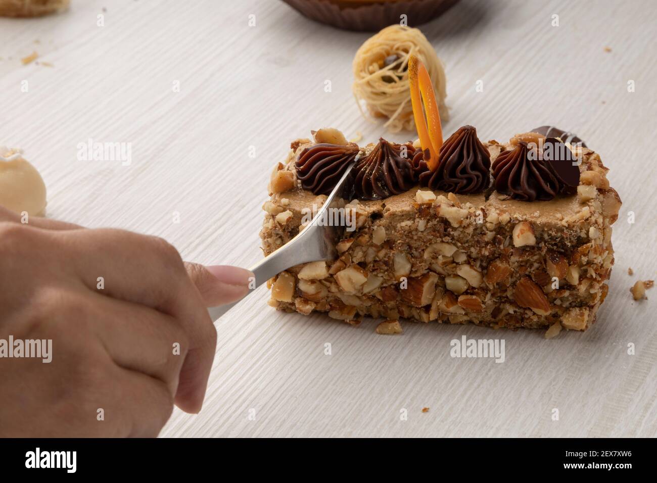 mano con forchetta tagliando un pezzo di torta ripieno di noce con decorazione al cioccolato, dessert in uno studio Foto Stock