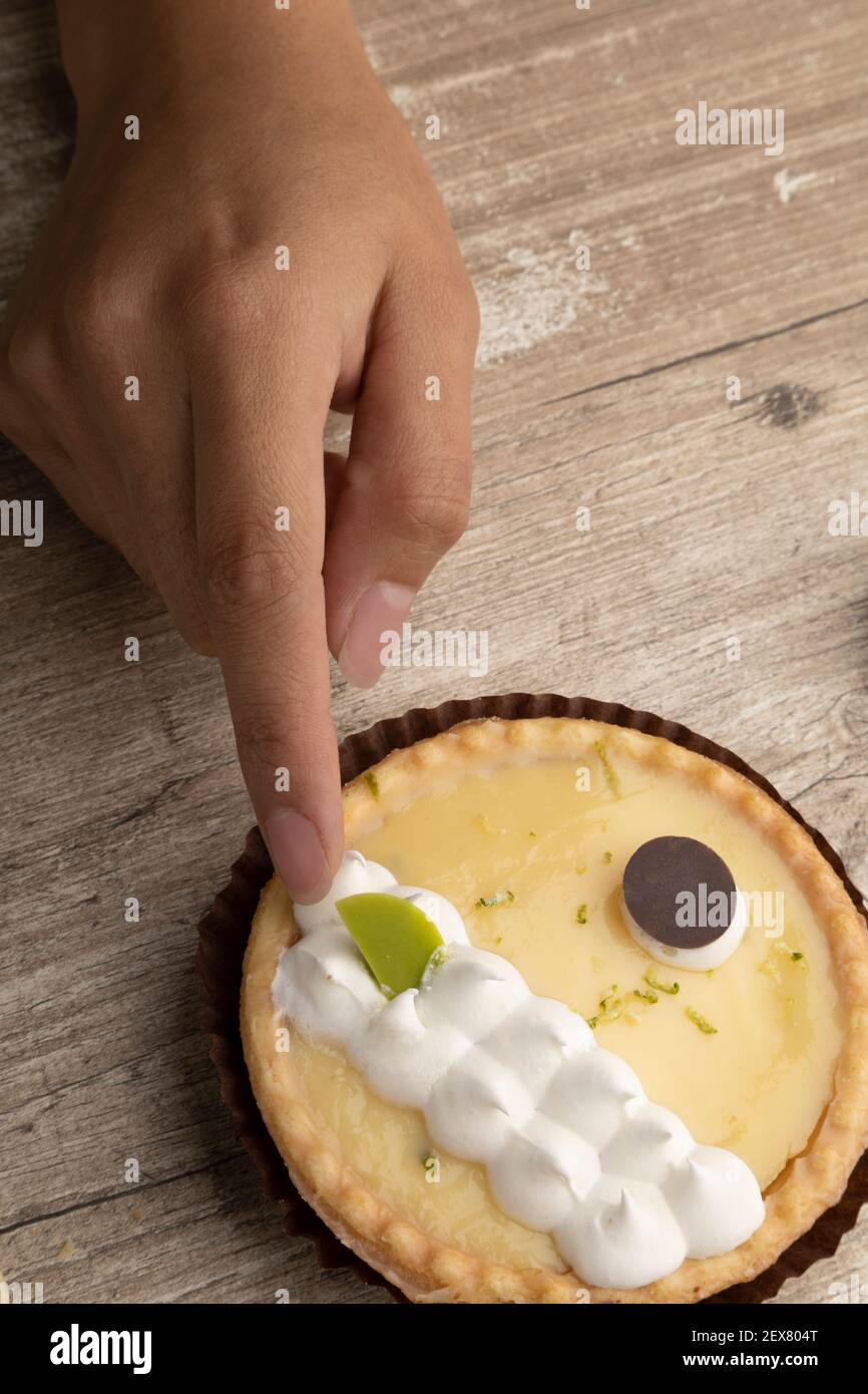 closeup di una mano che tocca la decorazione di una torta al limone, pasticceria in uno studio Foto Stock