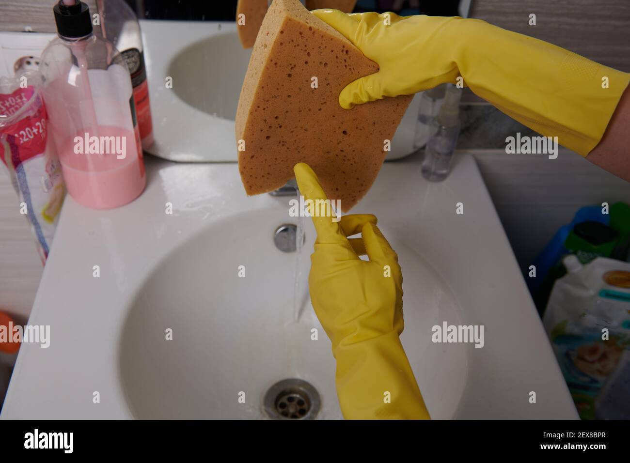 lavando la spugna nel lavandino con guanti gialli Foto Stock