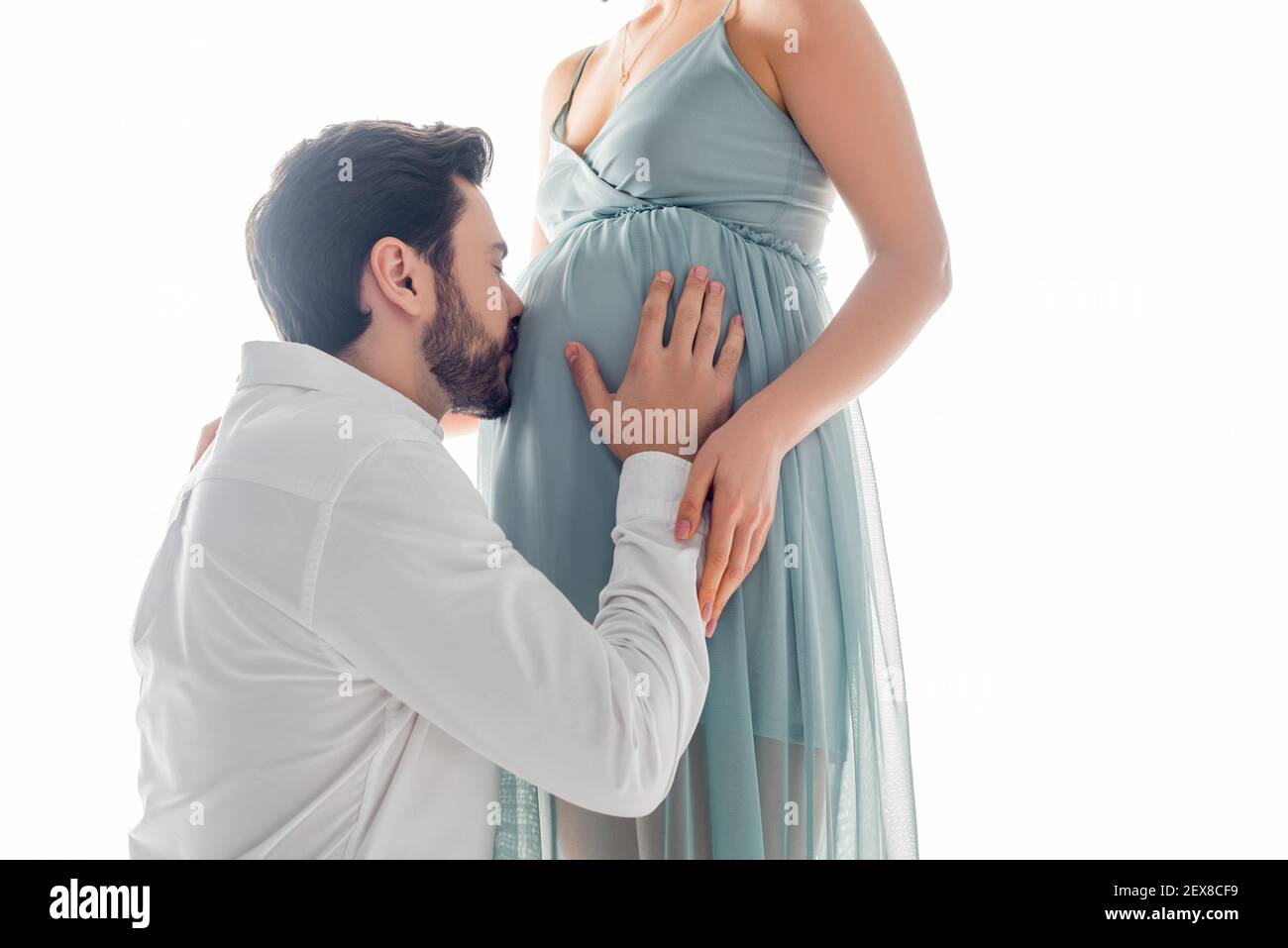 Giovane uomo baciando pancia di moglie incinta isolato su bianco Foto Stock
