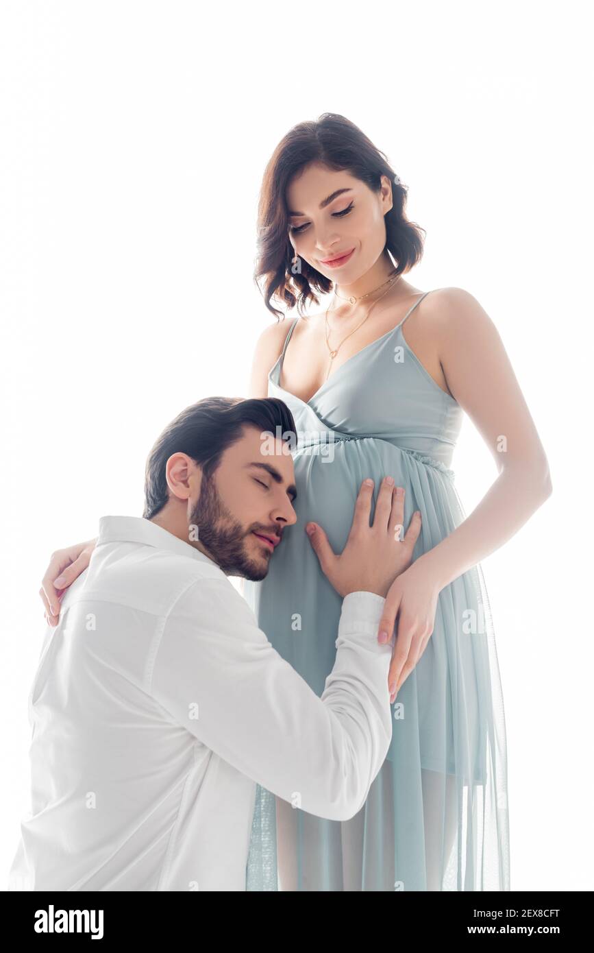 Uomo bearded che ascolta il ventre della moglie incinta isolato su bianco Foto Stock