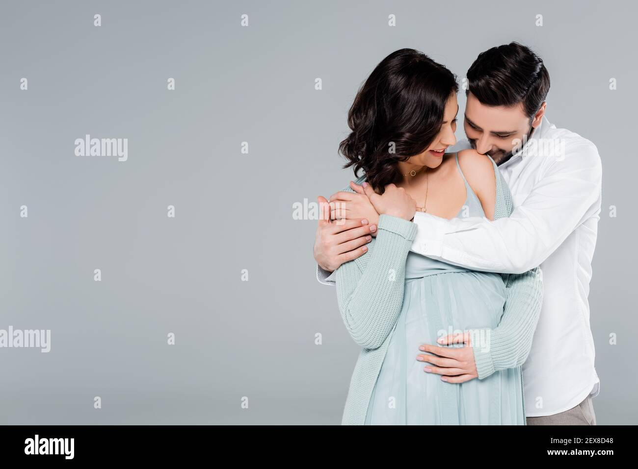 Uomo baciando la spalla della moglie incinta isolato su grigio Foto Stock