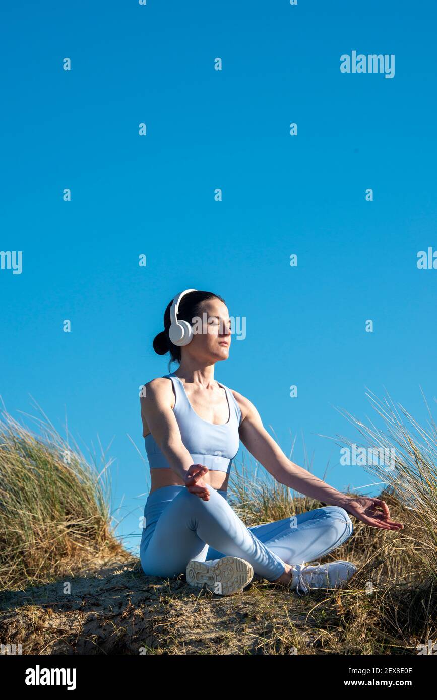 Donna che medita e ascolta musica fuori al sole. Indossare le cuffie. Foto Stock