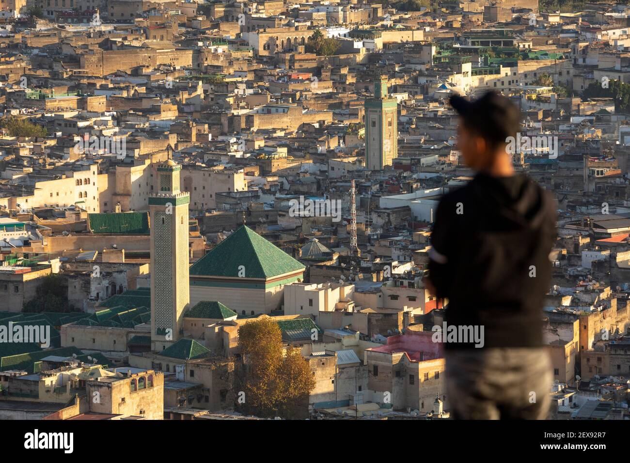 Un giovane uomo locale che si affaccia sulla Medina Fes al tramonto, mostrando la Moschea al Karaouine, come si vede dalle Tombe Marinide, Fes, Marocco Foto Stock