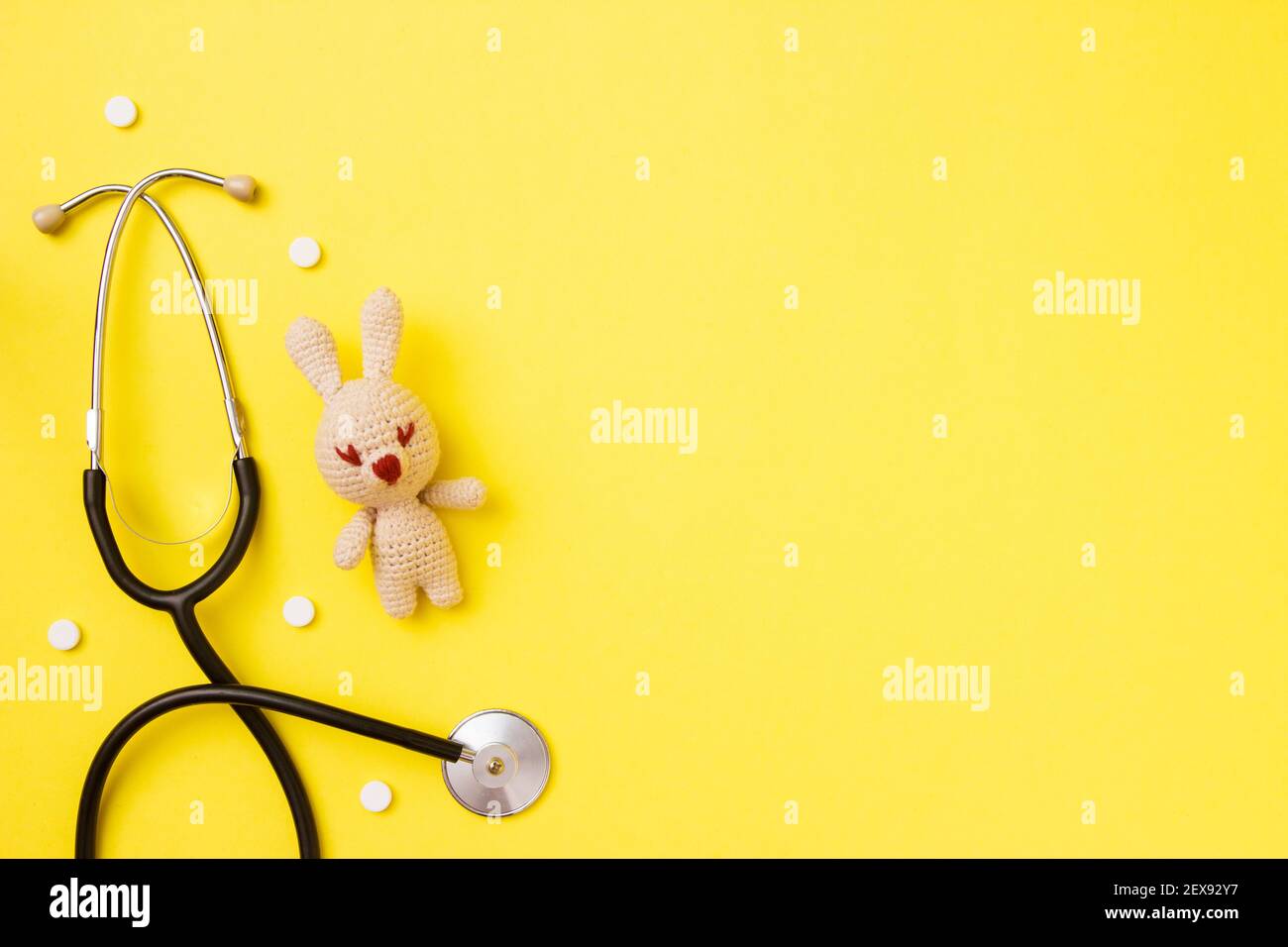 Amigurumi giocattolo per bambini con stetoscopio su sfondo giallo con spazio copia. Concetto di salute dei bambini. Vista dall'alto, disposizione piatta Foto Stock