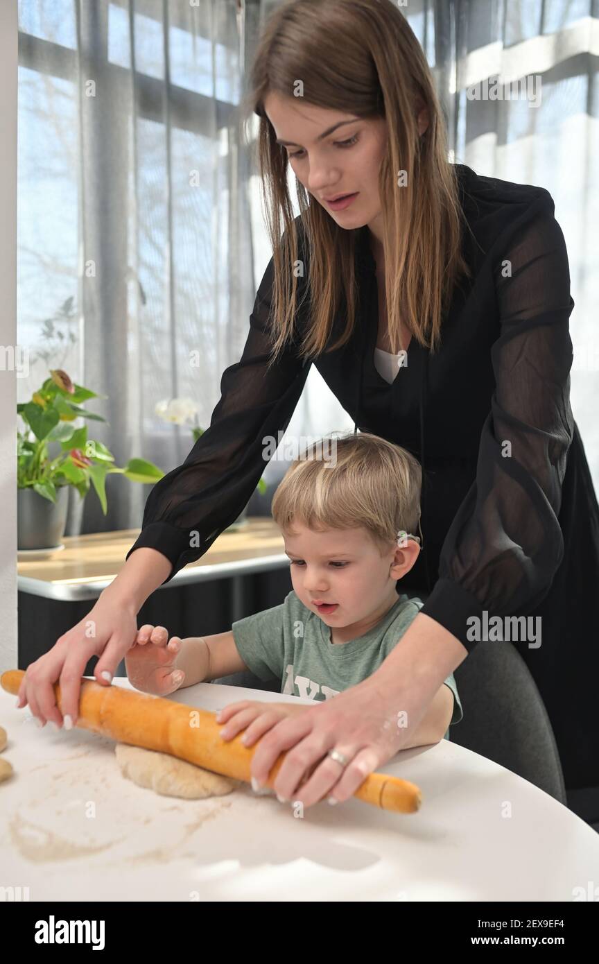 Madre con il figlio del toddler con gli impianti del coclear che cuoce le ciambelle sopra Cucina Foto Stock