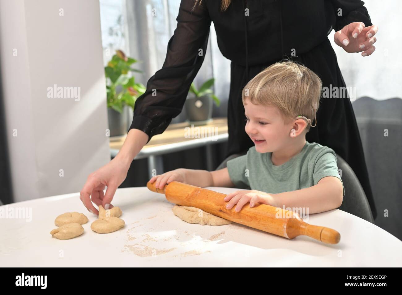 Madre con il figlio del toddler con gli impianti del coclear che cuoce le ciambelle sopra Cucina Foto Stock