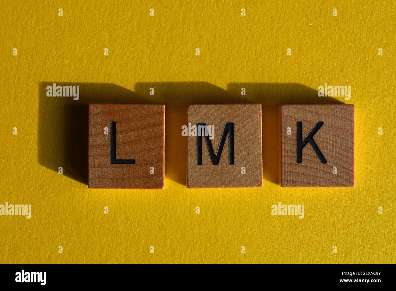 LMK, acronimo di Let Me Know, in lettere alfabetiche in legno isolate su sfondo giallo Foto Stock