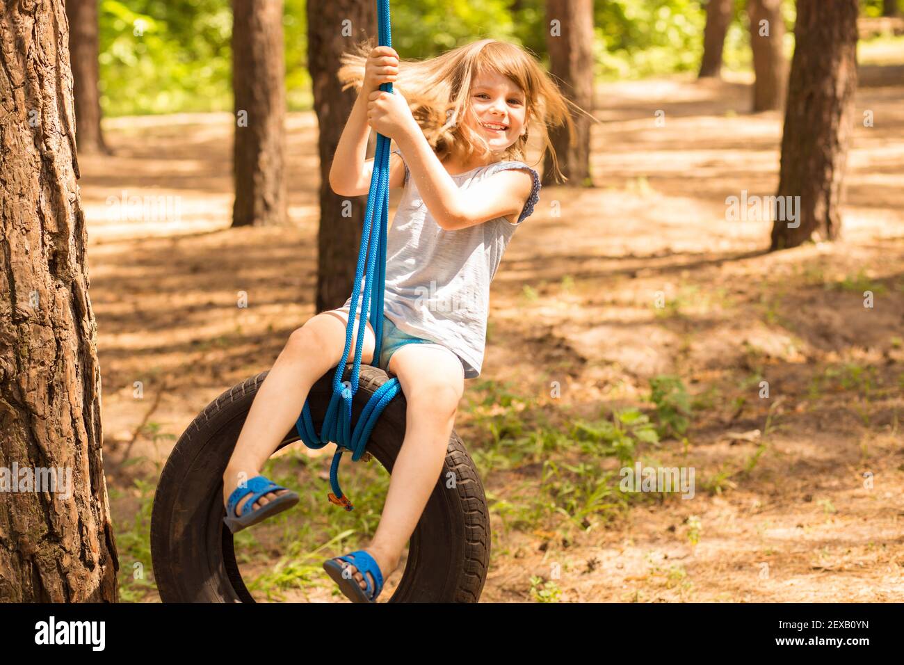 Carino bambina che oscilla sulla ruota attaccata al grande albero nella foresta di autunno. Foto Stock