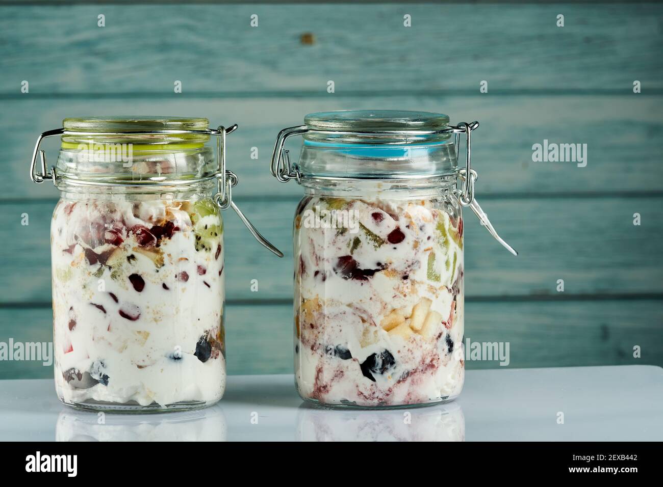 Due vasetti di yogurt fresco con frutta e bacche al suo interno su sfondo di legno blu. Foto Stock