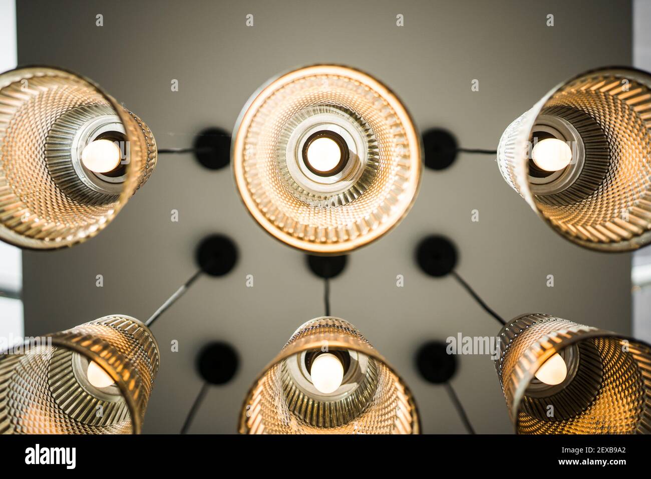 Guardando fino al soffitto, si accendono le luci simmetriche pensili acceso e luminoso con lampade in vetro sfumature in moderno nuovo edificio Foto Stock