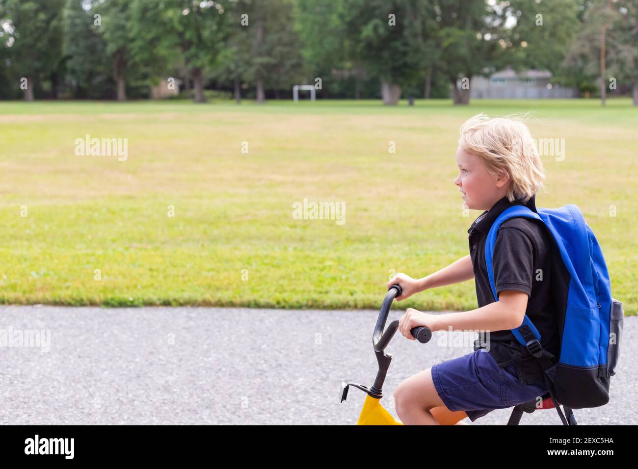Bambino che va a scuola in bicicletta. Studente con bici in cortile. Scuola campo di calcio e un ragazzo che cavalcano una bicicletta. Foto Stock