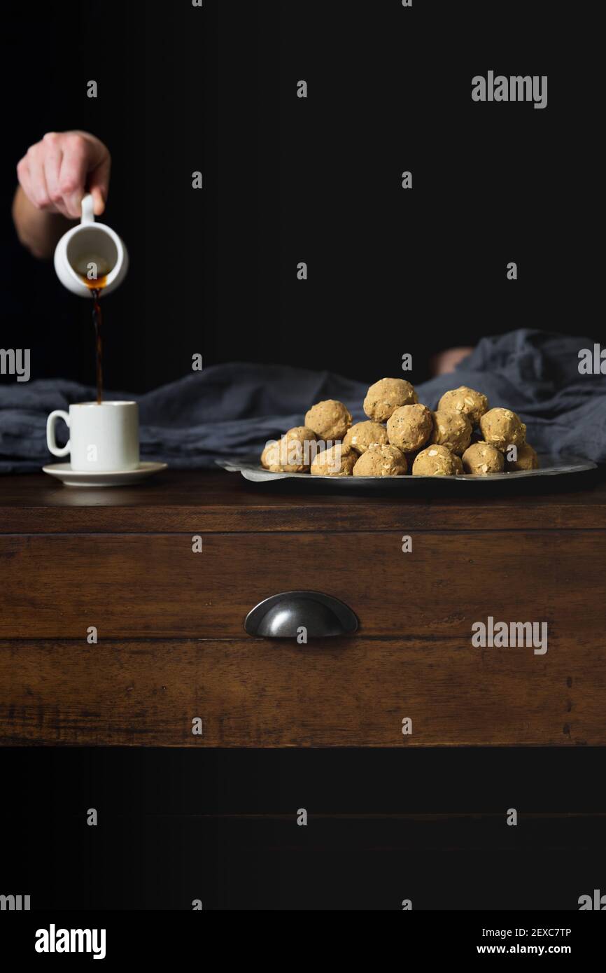 Una mano che tiene una caraffa versa il caffè in una tazza accanto a palle proteiche Foto Stock
