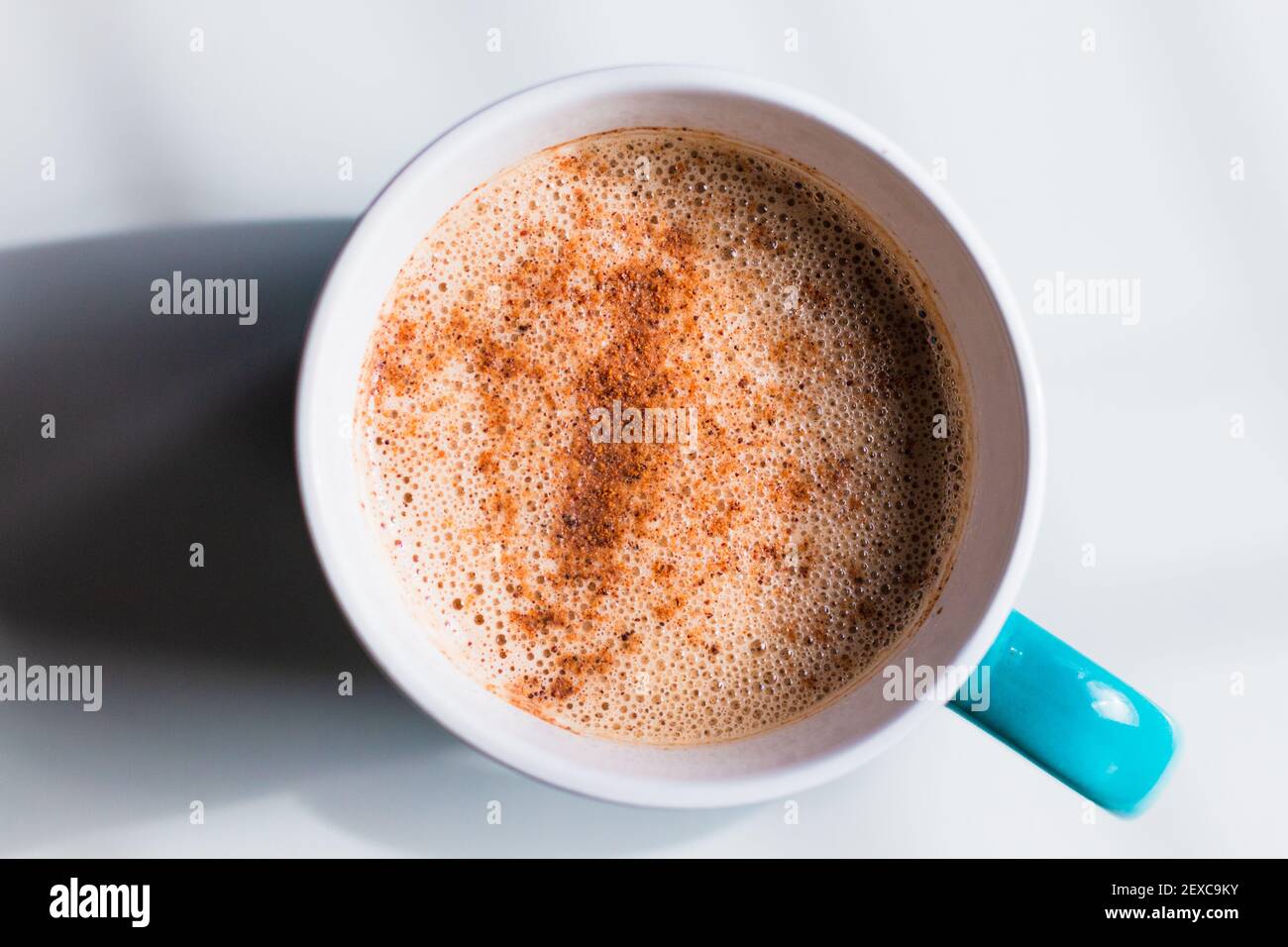 Piatto rigido e leggero di un latte di tè schiumoso, ricoperto di cannella in una tazza blu su una superficie bianca. Foto Stock