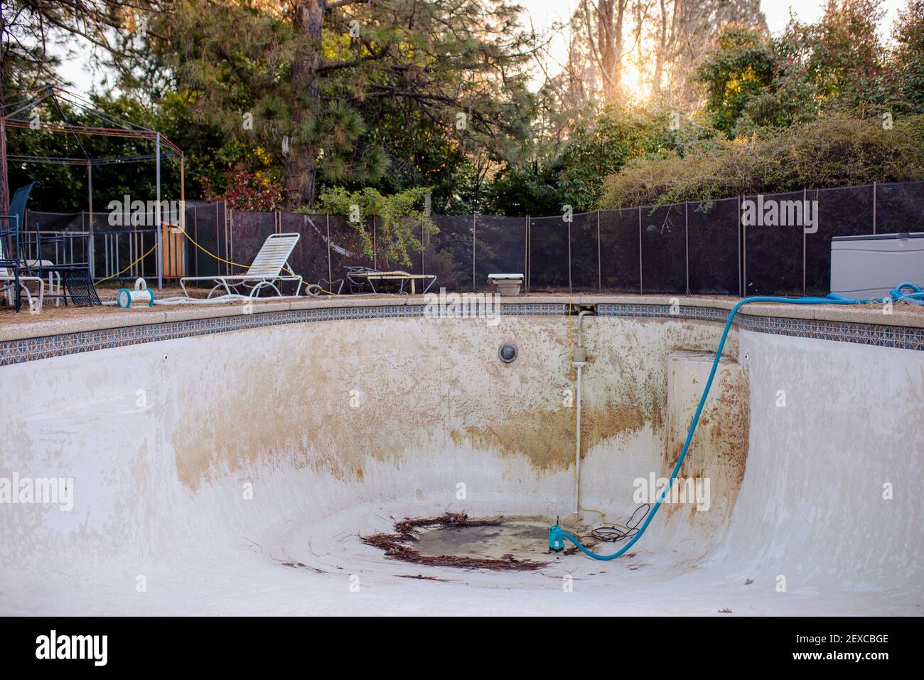 Vuoto in piscina a terra con puddle e attrezzatura di riparazione in Un cortile Foto Stock