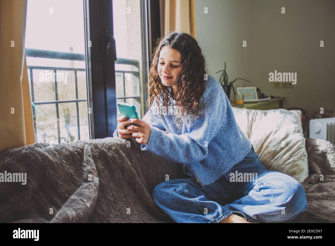 giovane donna che guarda il cellulare sul divano vicino la finestra Foto Stock