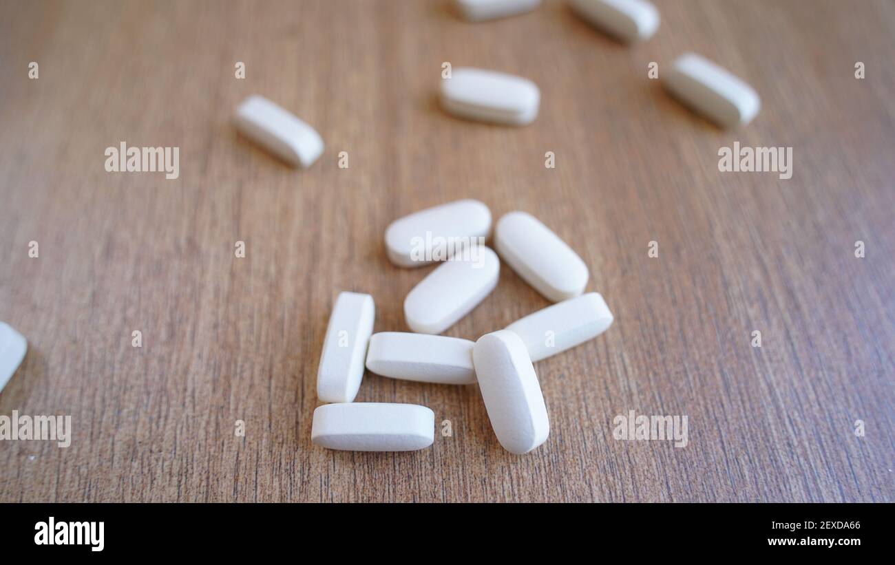 Cumulo di calcio, vitamina supplemento compresse isolato su sfondo di legno. Molte pillole mediche bianche e capsule per ossa forti. Rimani al sicuro e tieniti in salute Foto Stock