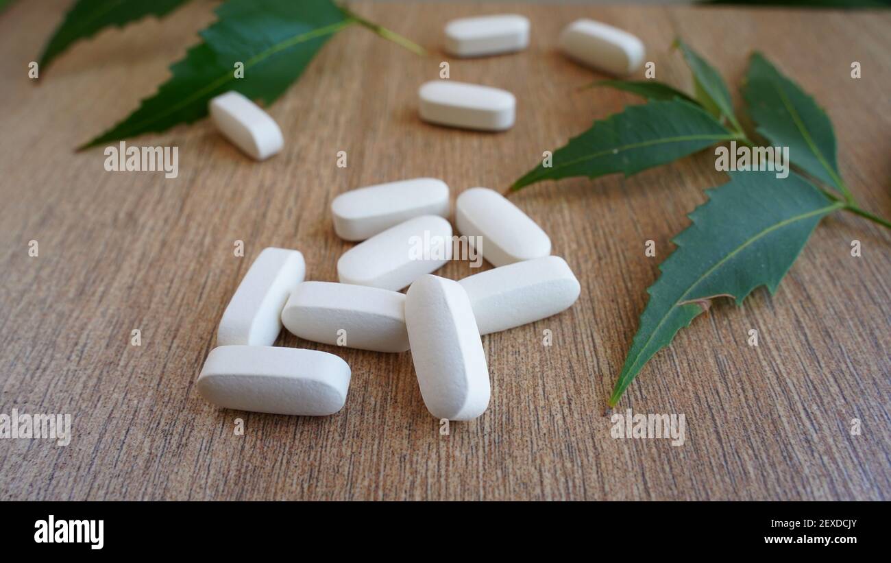 Cumulo di calcio, vitamina supplemento compresse con foglia di starnuto isolato su sfondo di legno. Molte pillole mediche bianche e capsule per ossa forti. Rimani Foto Stock