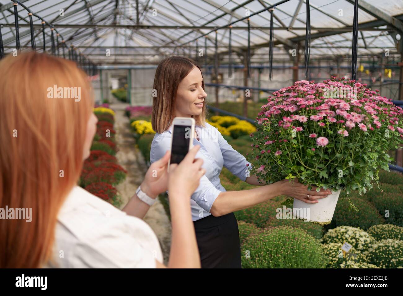 Instagram fotografo blogging workshop concetto. Primo piano le mani delle donne che tengono il telefono e scattano foto della ragazza con i fiori. Messa a fuoco selettiva. Foto Stock