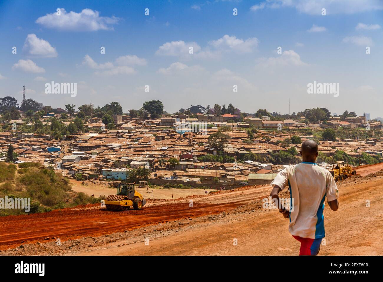 Un uomo africano corre per l'esercizio su una strada sterrata accanto a una parte della baraccopoli di Kibera a Nairobi, Kenya. Foto Stock