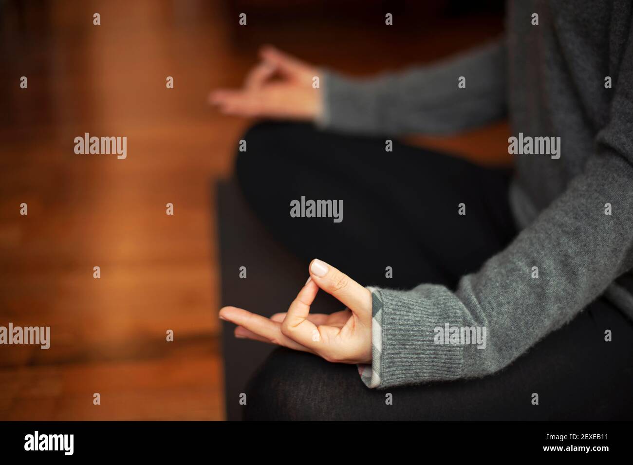 Primo piano delle mani della donna, seduta sul pavimento a gambe incrociate, posizione sukhasana / loto. Pratica quotidiana di meditazione, salute mentale, concetto di stile di vita yoga Foto Stock