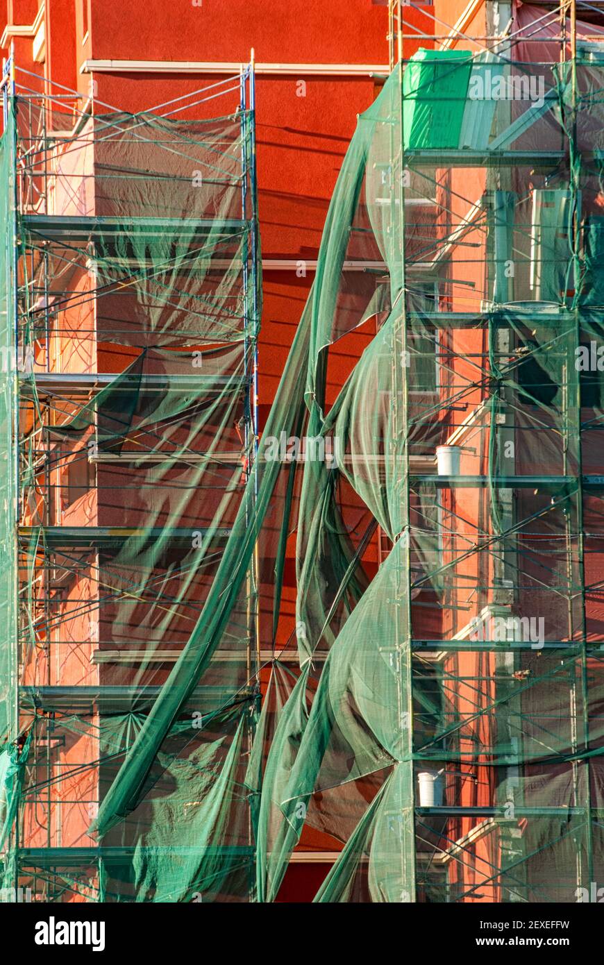 Un edificio rosso con impalcature racchiuse nel verde tessuto di sicurezza Foto Stock