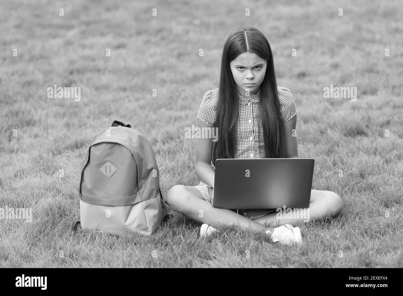 sconvolto il bambino mentre si usa il computer sedersi su erba verde nel parco con borsa della scuola, educazione infantile. Foto Stock