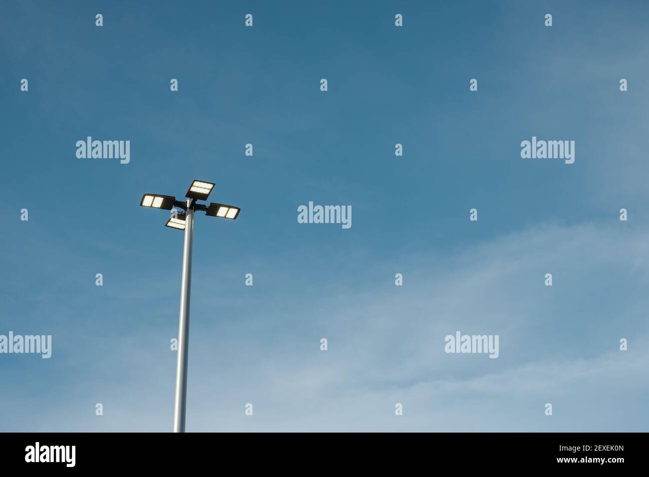 Vista ad angolo basso delle luci di strada su un palo. Il gruppo di quattro luci è visto contro un cielo blu con nuvole bianche opacizzanti. Foto Stock