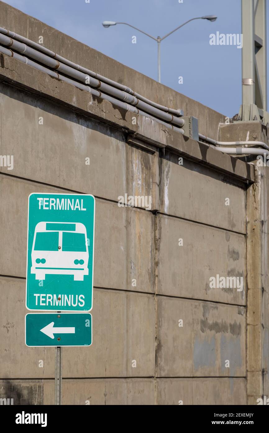 Un cartello verde bilingue, in inglese e francese, punta a sinistra in direzione di un terminal della stazione degli autobus. Un muro di cemento sul lato di un'autostrada si erge Foto Stock