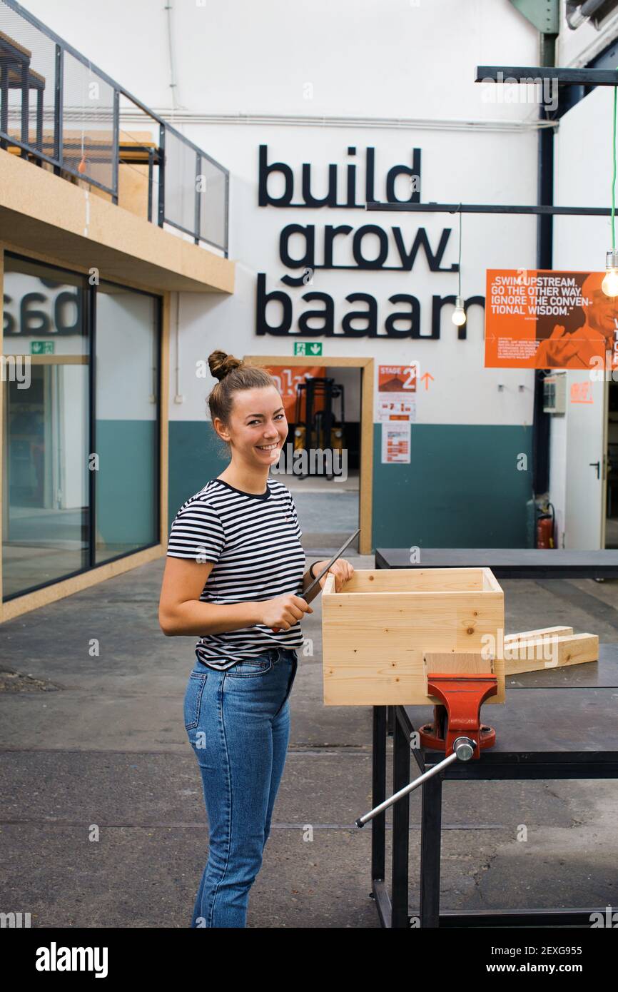 Carpentiere femminile piuttosto giovane che forma la superficie di legno di legno Cassa nello spazio di produzione urbano Tattcraft a Francoforte, Germania Foto Stock