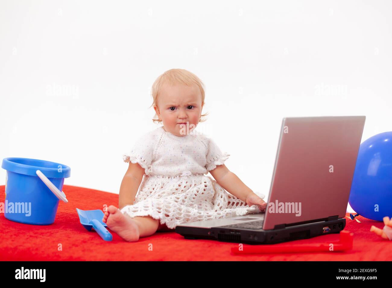 Ragazza seria del bambino in vestito lavorato bianco si siede dietro a. computer portatile tra i giocattoli Foto Stock