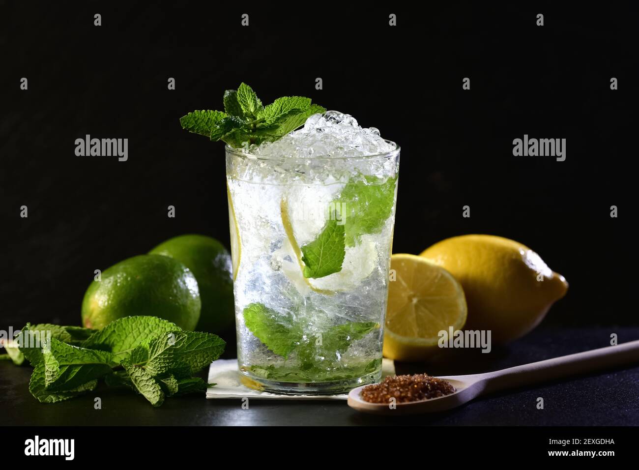 Messa a fuoco selettiva e primo piano di un cocktail mojito con foglie di menta, lime, limoni e un cucchiaio di legno con zucchero di canna. Ingredienti freschi. Foto Stock