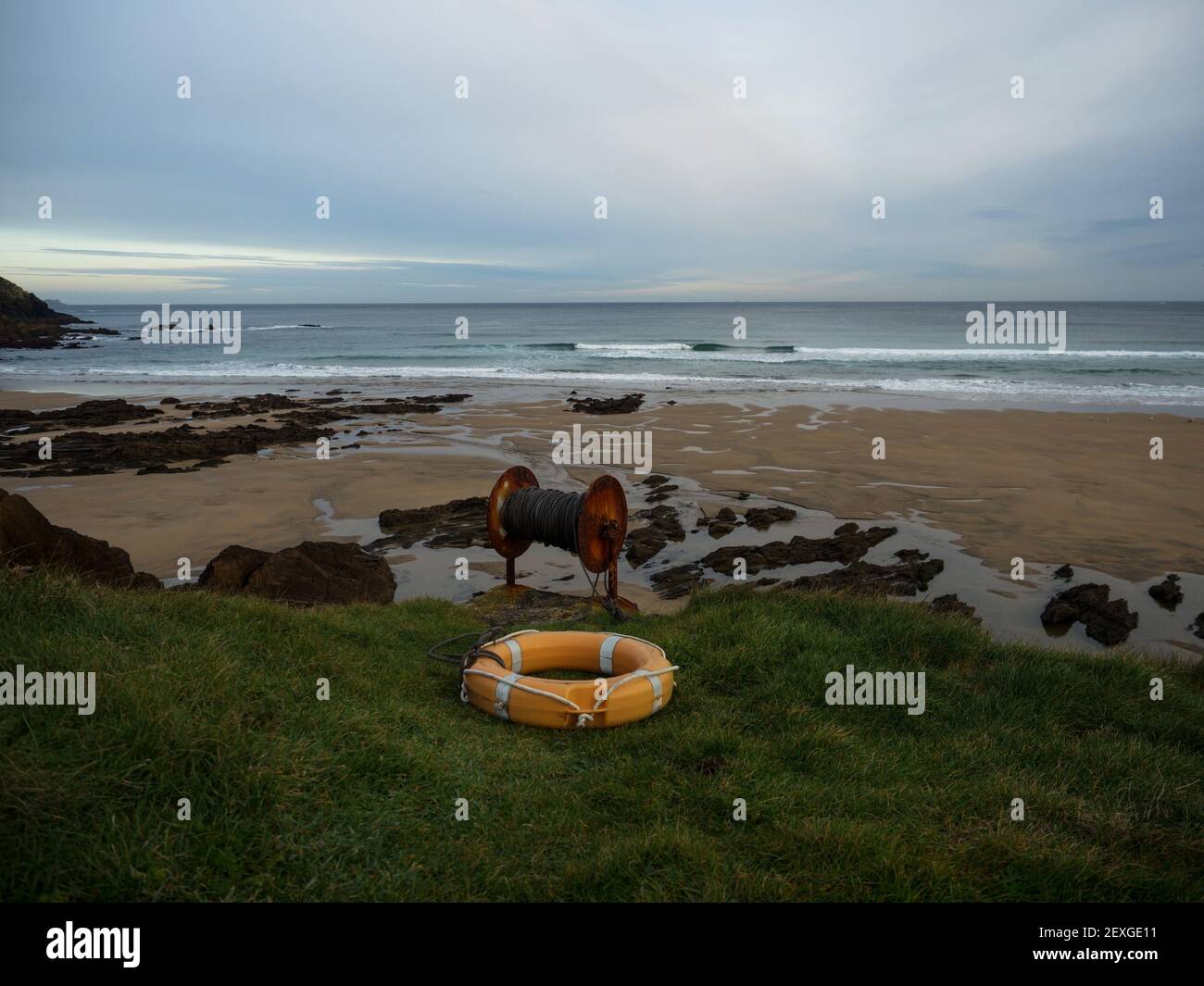 Cintura salvagente arancione con corda annegata rischio di salvataggio galleggiante Adagiato in erba verde sulla spiaggia della costa atlantica Praia dos Rias a Malpica de Be Foto Stock