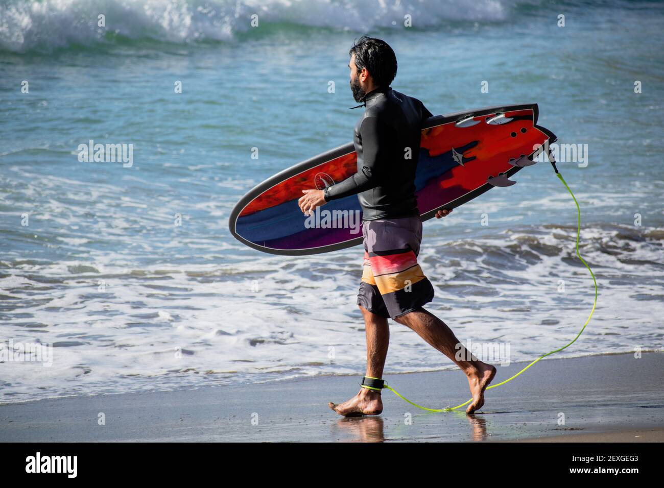 AUCKLAND, NUOVA ZELANDA - 21 febbraio 2021: Vista del surfer con il surf colorato che entra in acqua alla spiaggia di Piha, Auckland, Nuova Zelanda Foto Stock