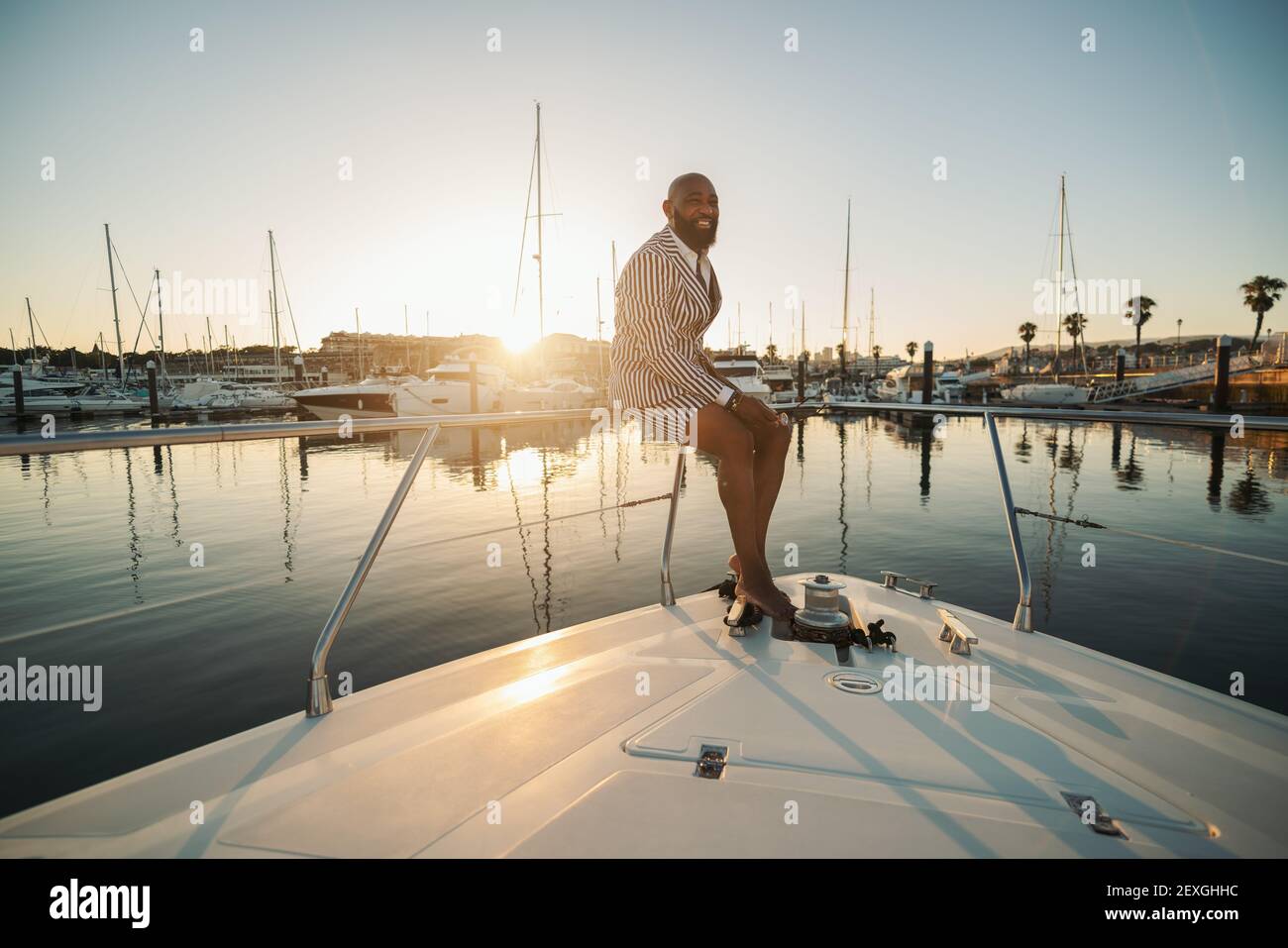 Un allegro ed elegante baldo maturo sopportato uomo nero in un tuta estiva composta da shorts a righe e blazer è seduto sulle ringhiere del suo lusso Foto Stock