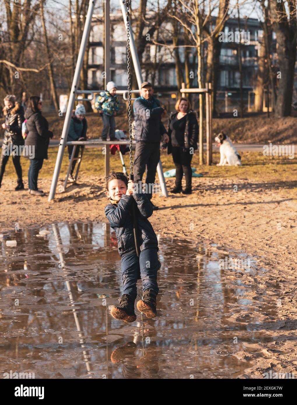 POZ, POLONIA - 21 febbraio 2021: Giovane ragazzo caucasico polacco felice che tiene su una zipline attrezzatura in un parco giochi nel Solacki parco con grande acqua puddle Foto Stock